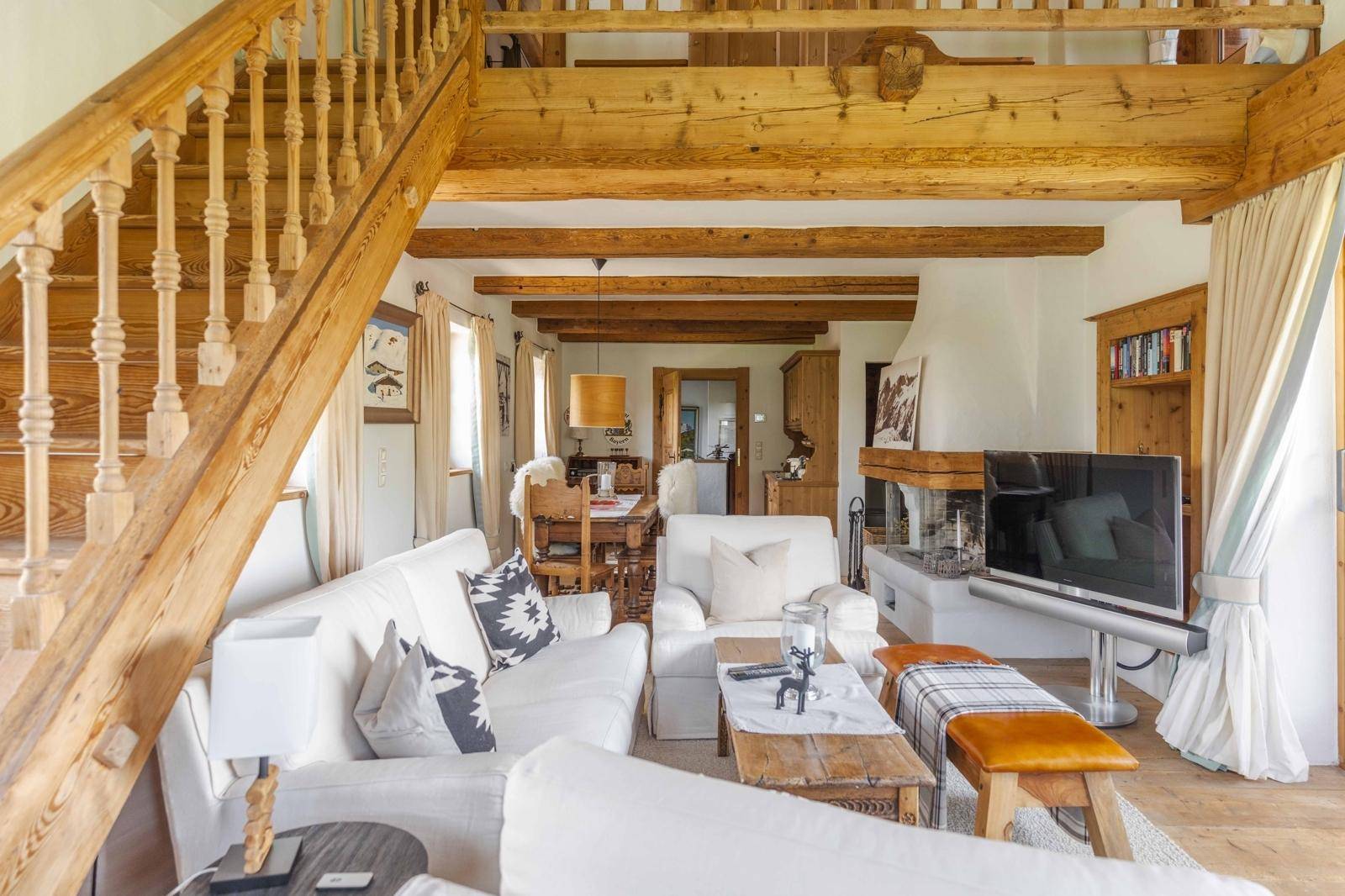 Helles Wohnzimmer mit Holzbalken, bequemen Sofas und einer Holztreppe, die in die obere Etage führt.