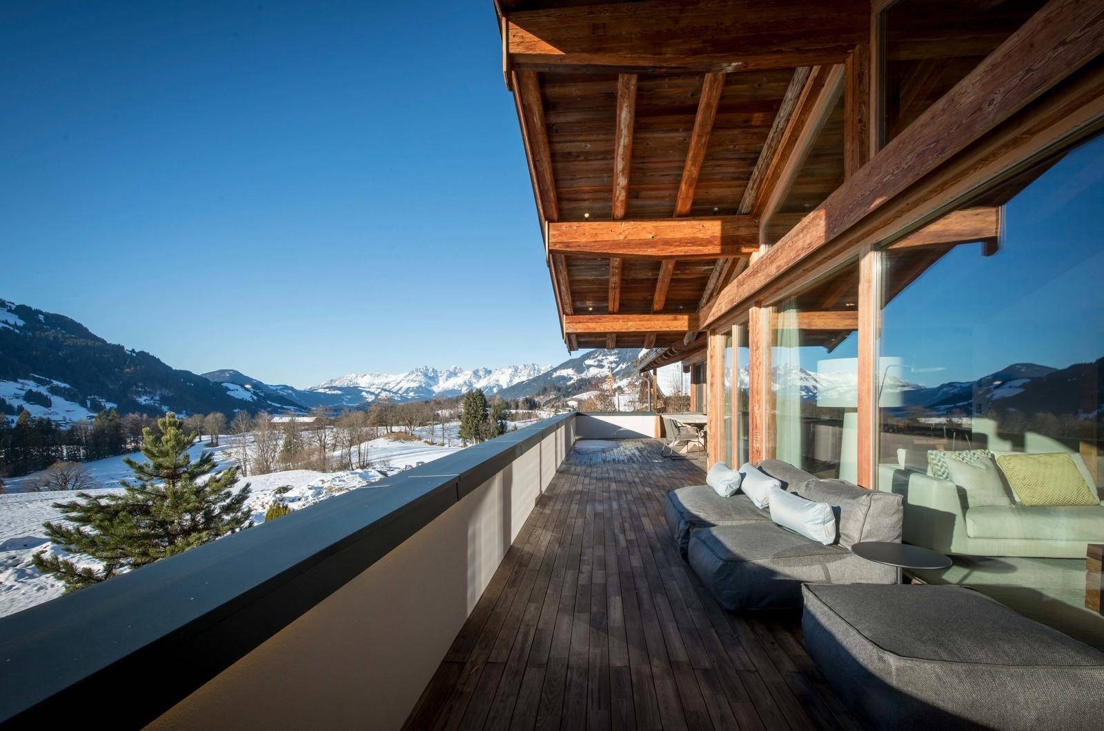 Geräumiger Holzbalkon mit bequemen Lounge-Möbeln und atemberaubendem Panoramablick auf die verschneiten Berge.
