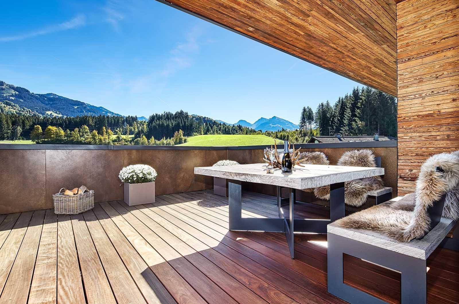Geräumige Terrasse mit Holzboden, Esstisch und Bergblick, umgeben von grüner Natur.