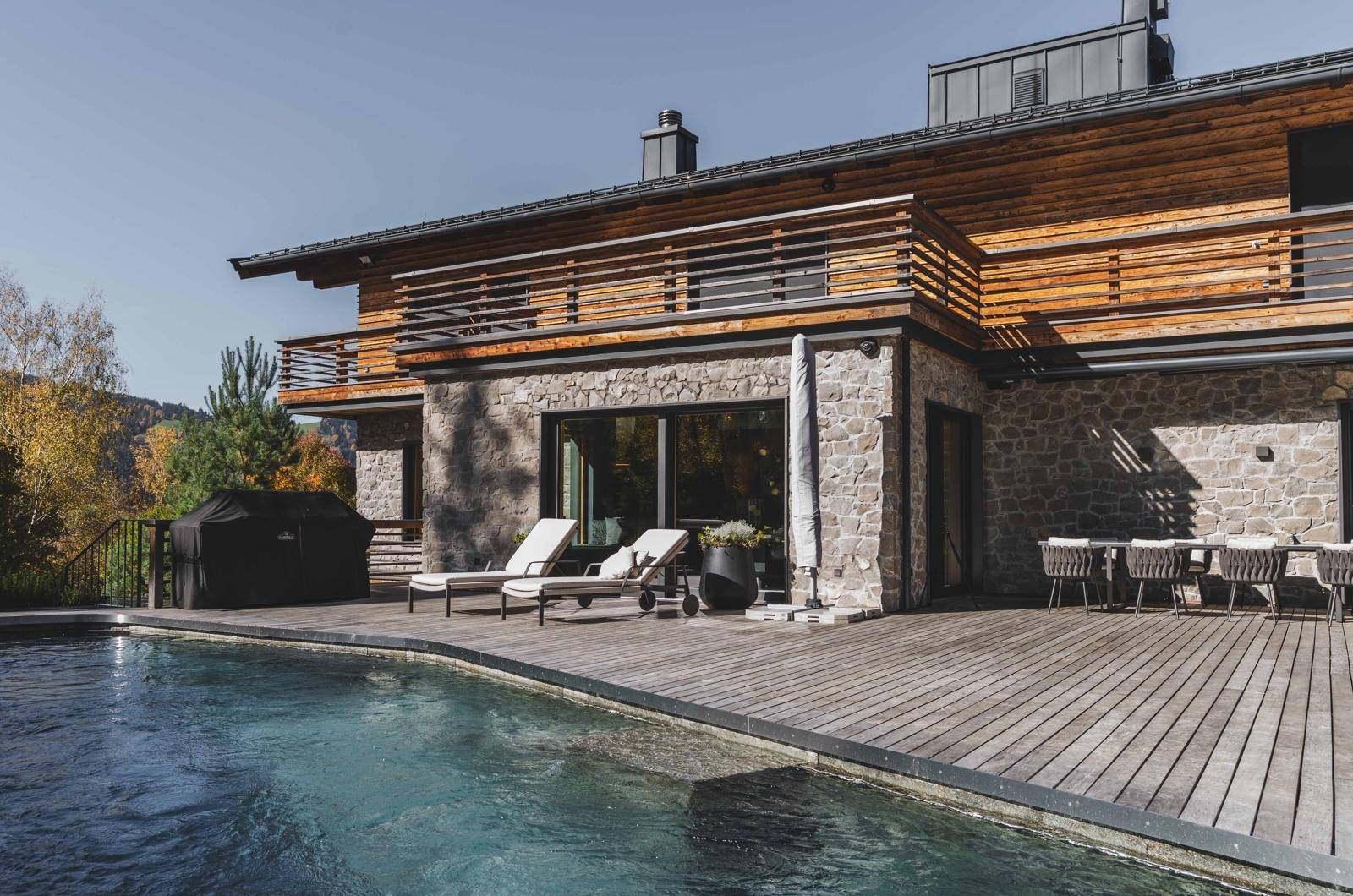 Großzügige Holzterrasse mit Pool, Sonnenliegen, Grillbereich und Esstisch, ideal für Entspannung im Freien.