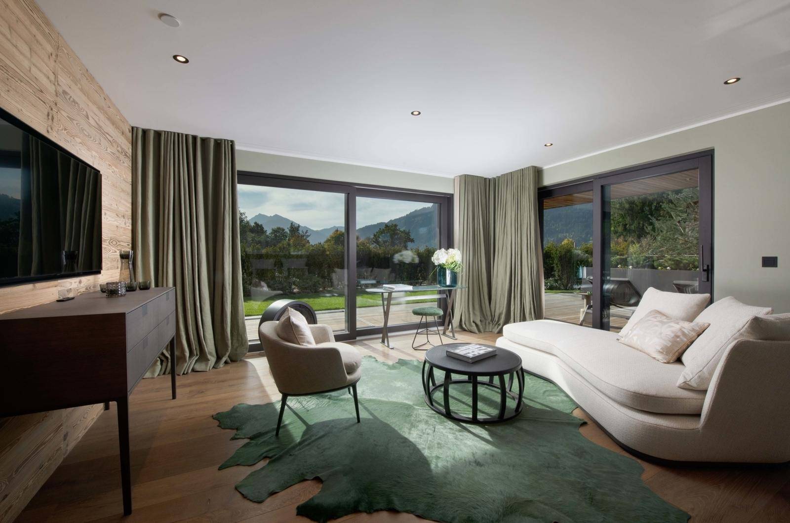 Modernes Wohnzimmer mit großen Fenstern, die einen weiten Bergblick bieten, Holzwand und stilvoller Einrichtung.