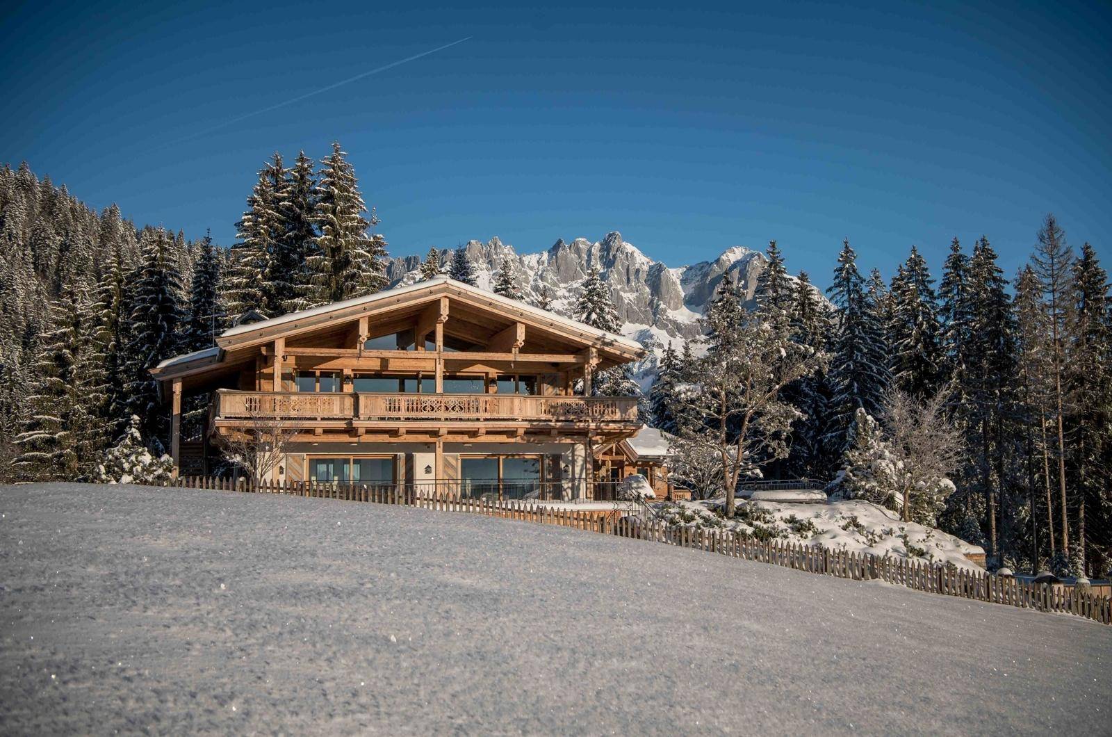 Idyllisches Holzchalet in winterlicher Bergkulisse mit verschneiten Bäumen und klarem Himmel.