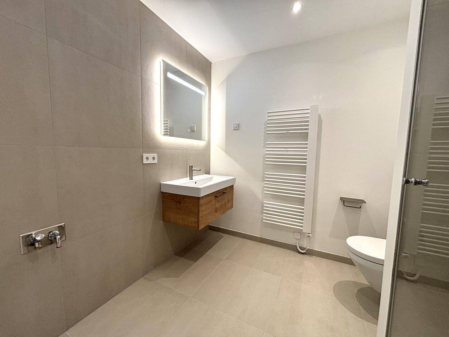 Modernes Badezimmer mit schwebendem Waschtisch, beleuchtetem Spiegel und Handtuchheizkörper.