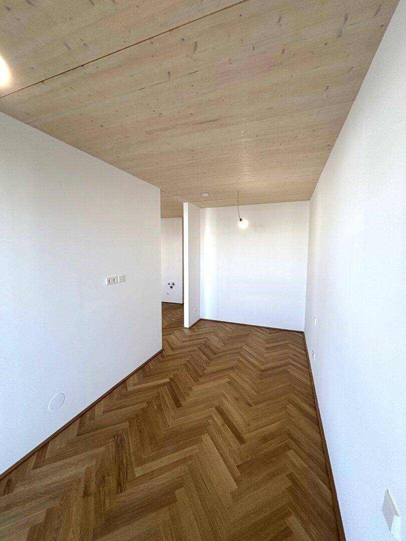 Heller Raum mit Fischgrätparkett und Holzdecke, bereit für die individuelle Gestaltung.