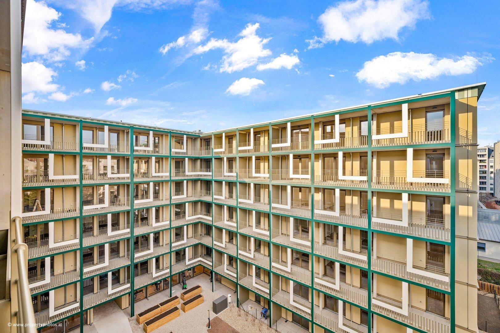 Innenhof eines modernen Wohnkomplexes mit vielen Balkonen und grünen Akzenten.