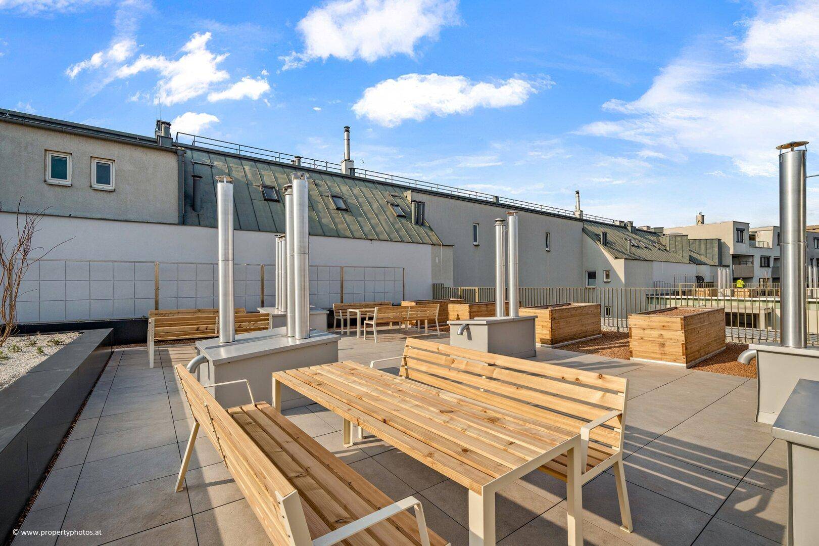 Geräumige Dachterrasse mit Holzbänken, Tischen und Blick auf die umliegenden Gebäude.