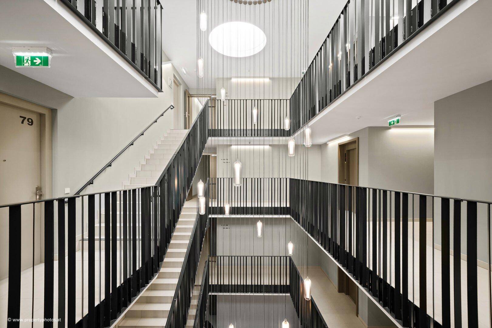 Mehrstöckiges Treppenhaus mit modernen Hängelampen und schwarzem Geländer.