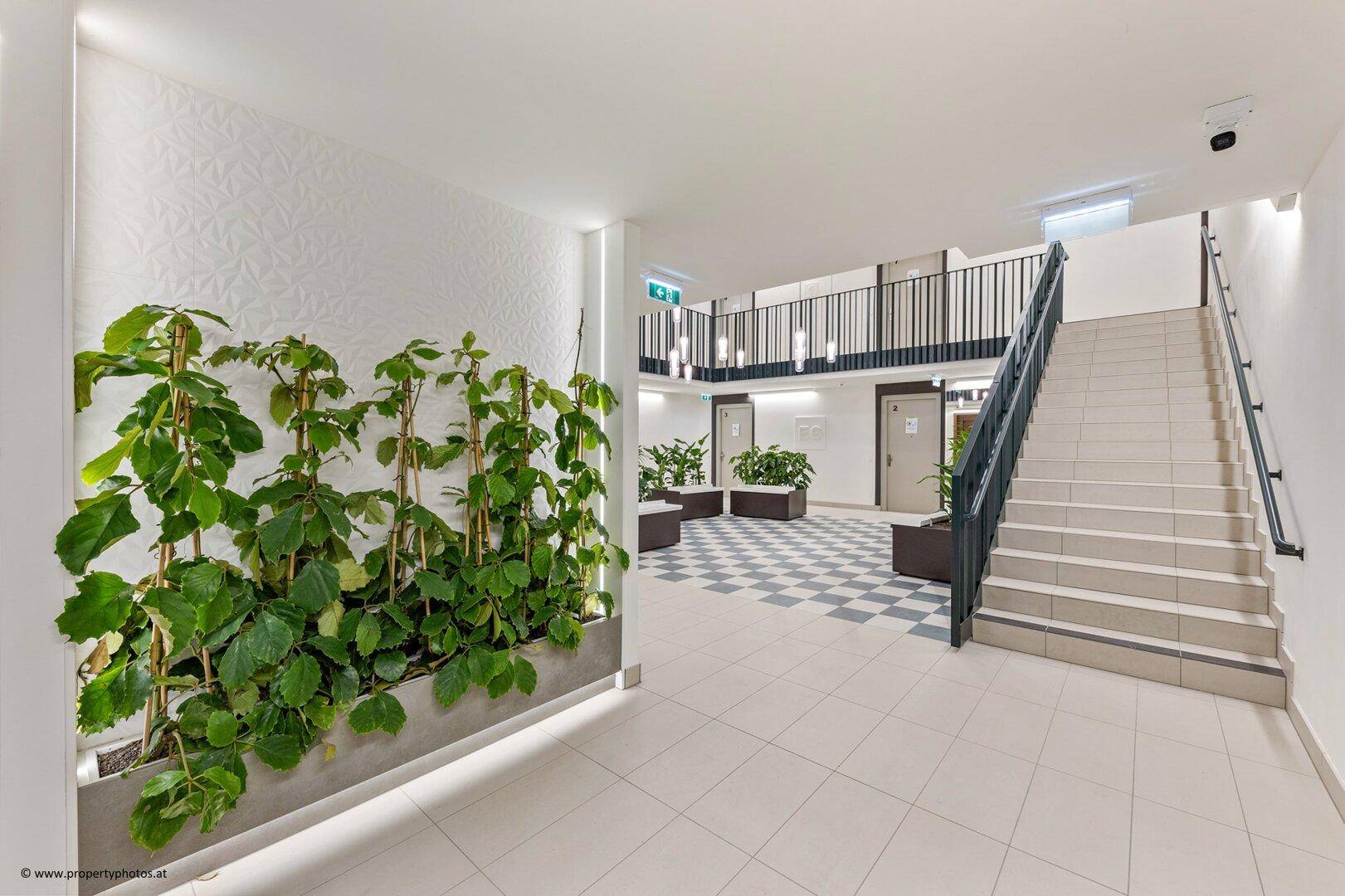 Geräumiger Flur mit Treppenaufgang, modernen Fliesen und integrierten Pflanzenbeeten für eine grüne Atmosphäre.
