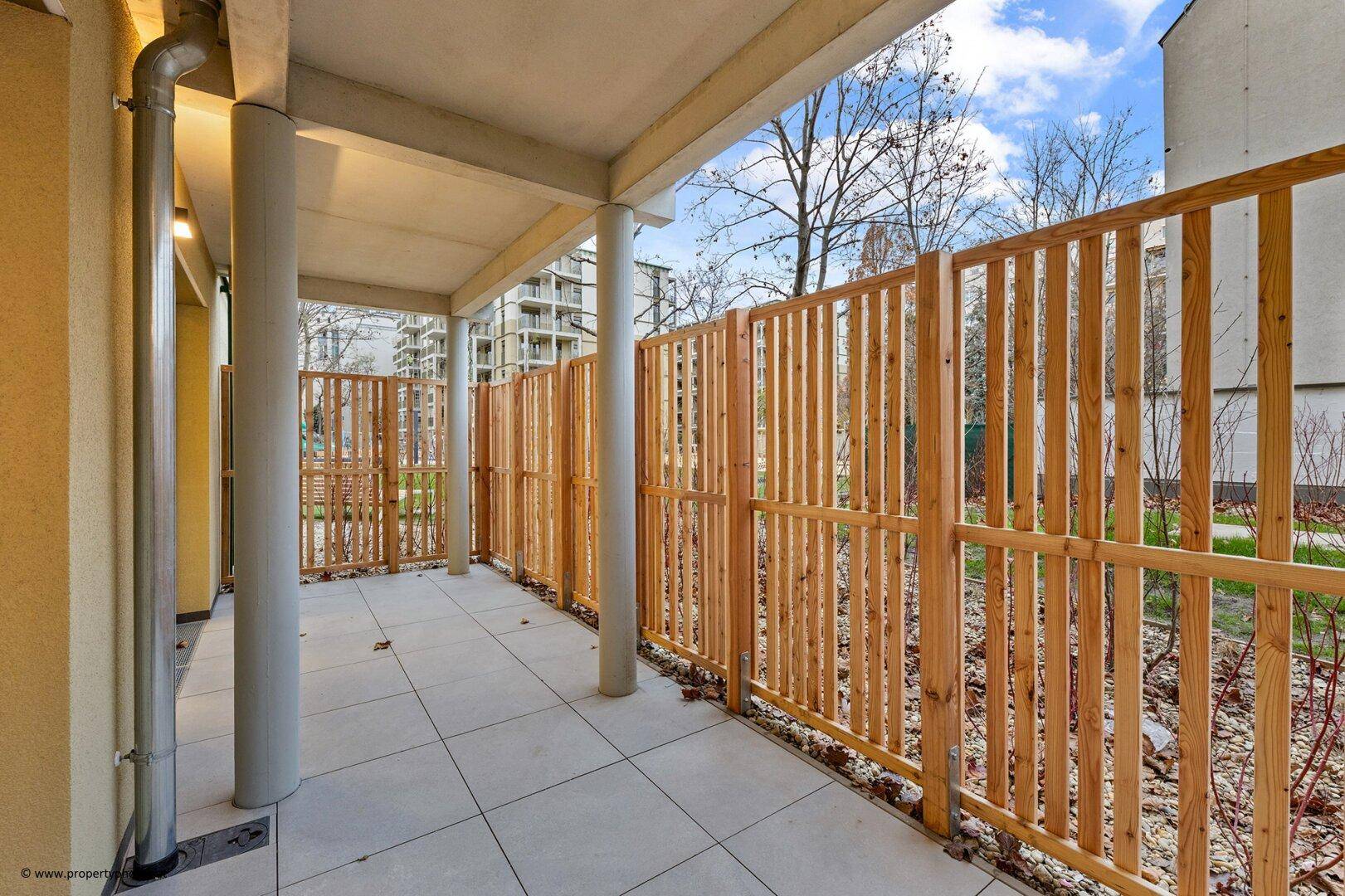 Überdachte Terrasse mit Fliesenboden und einem hohen Holzzaun für Privatsphäre im Freien.