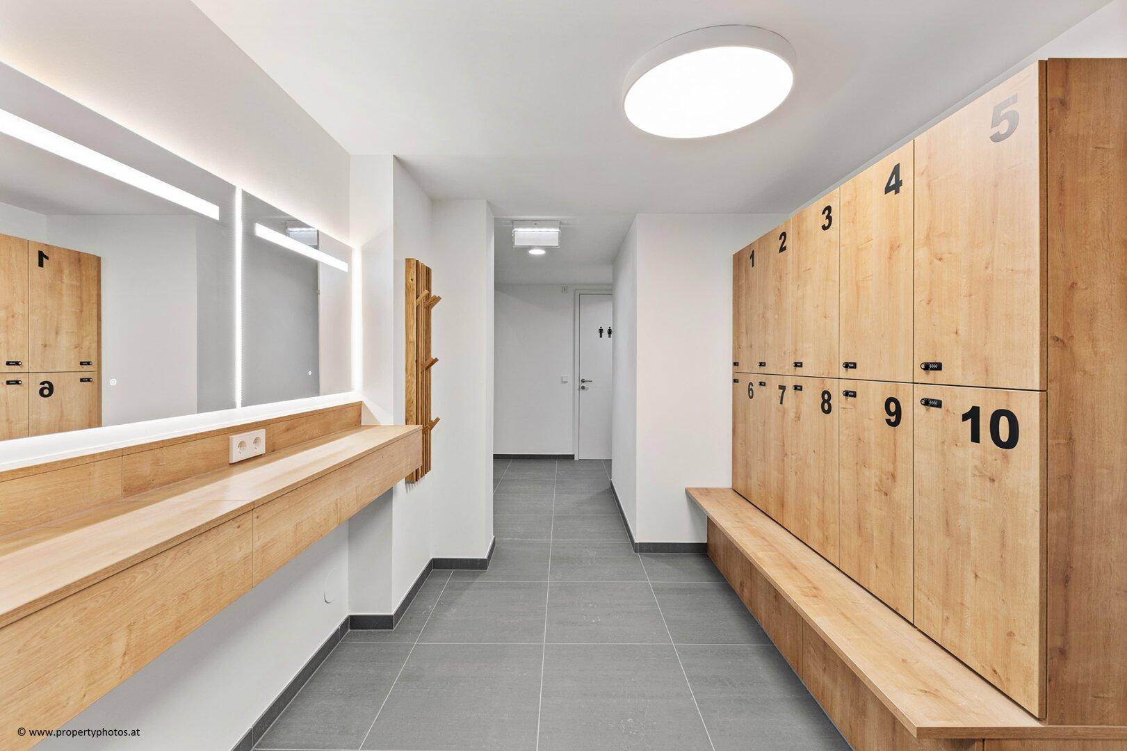 Heller Umkleideraum mit Holzkabinen, Sitzbänken und großem Spiegel für Sportler.