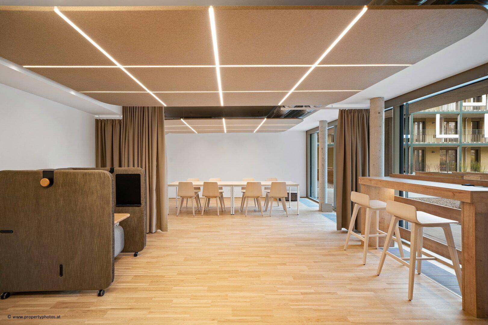 Großer Gemeinschaftsraum mit Holzboden, modernen Sitzgelegenheiten und integrierter Deckenbeleuchtung.