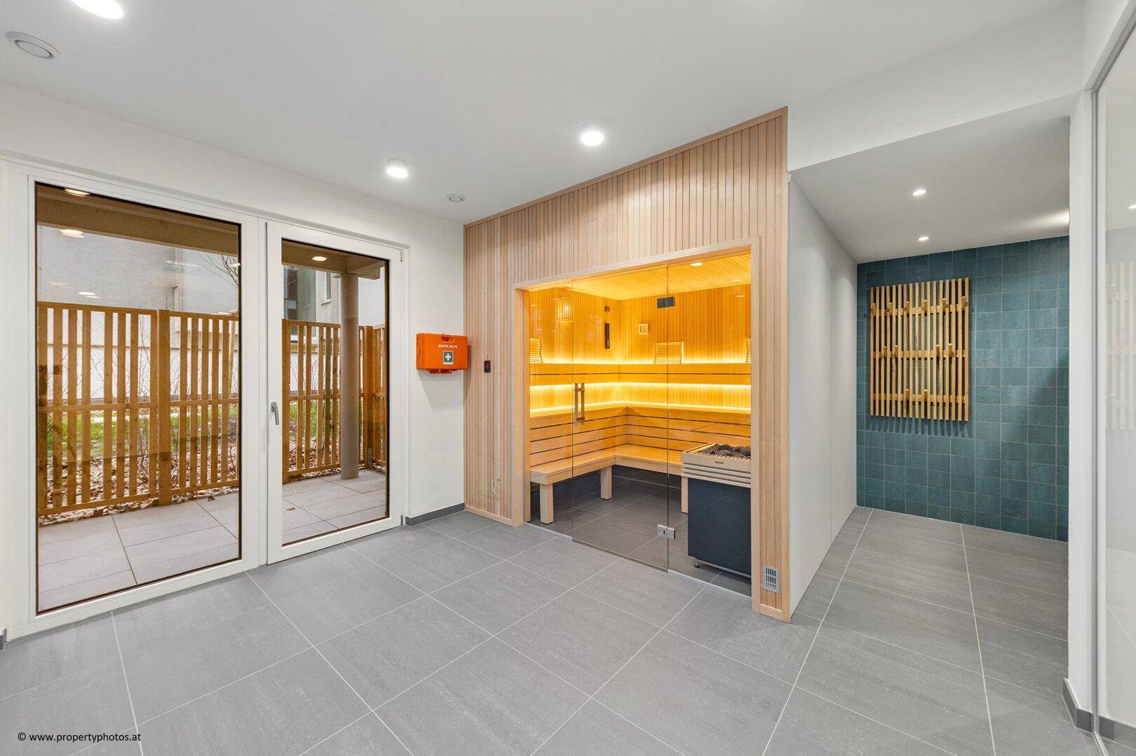Heller Wellnessbereich mit integrierter Sauna, Fliesenboden und Zugang zu einem Außenbereich.