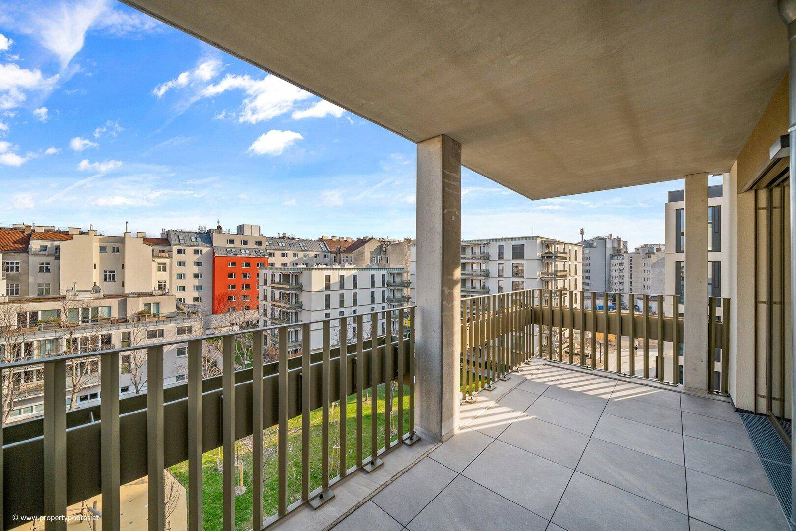 Geräumiger Balkon mit Fliesenboden und weitem Blick über die Stadt und umliegende Gebäude.