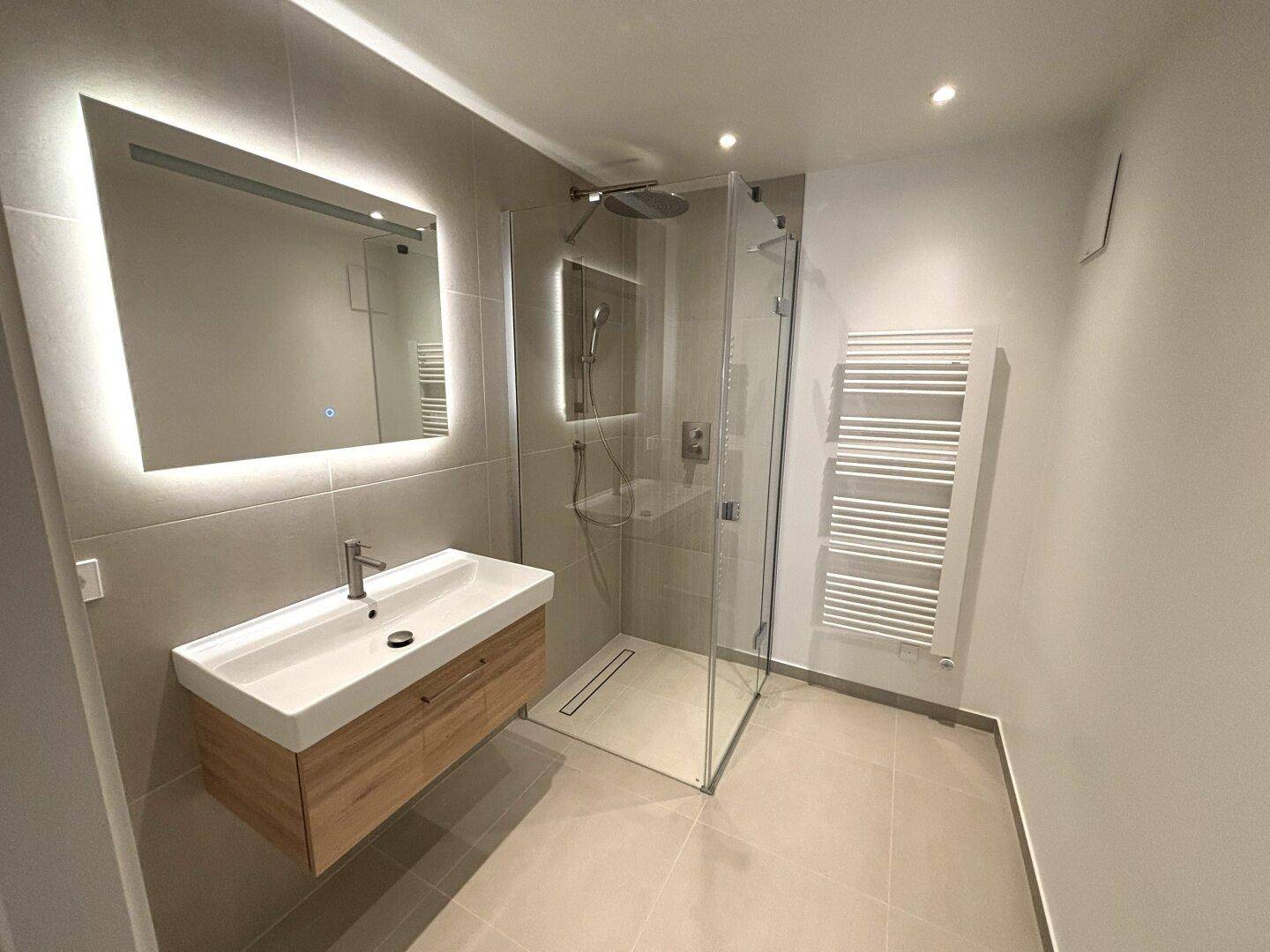 Modernes Badezimmer mit begehbarer Dusche, beleuchtetem Spiegel und Handtuchheizkörper.