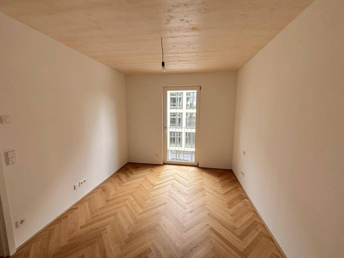 Helles Zimmer mit Fischgrätparkett und Zugang zu einem französischen Balkon.