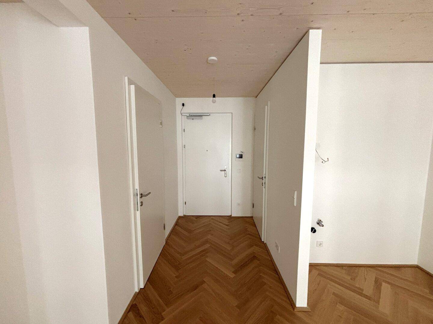 Heller Flur mit Fischgrätparkettboden und mehreren weißen Türen zu angrenzenden Räumen.