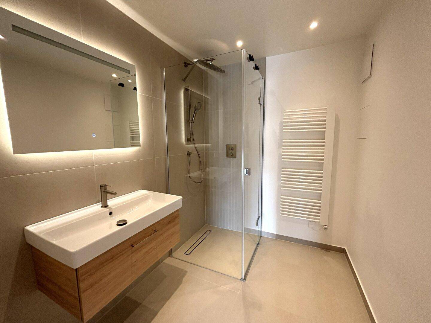 Modernes Badezimmer mit begehbarer Dusche, Einzelwaschbecken und beleuchtetem Spiegel.