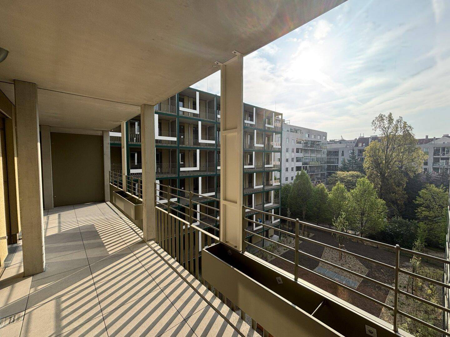 Sonniger Balkon mit Fliesenboden und Blick auf die umliegenden Wohngebäude und Grünflächen.