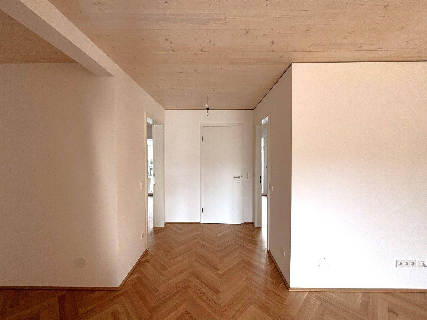 Geräumiger Eingangsbereich mit Fischgrätparkett und Holzdecke, der verschiedene Zimmer verbindet.