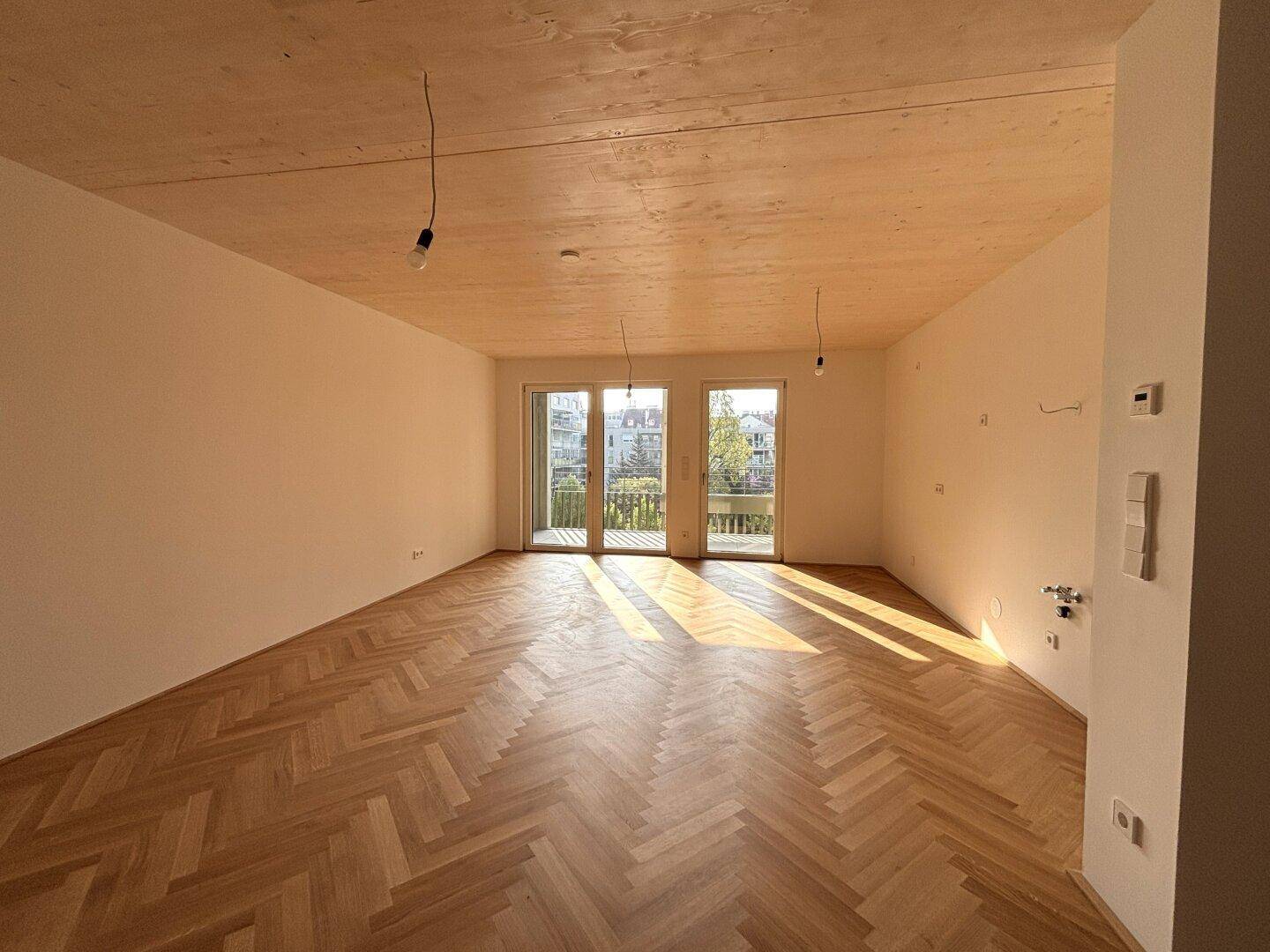 Geräumiger, heller Raum mit Fischgrätparkett, Holzdecke und viel natürlichem Licht durch die Balkontüren.