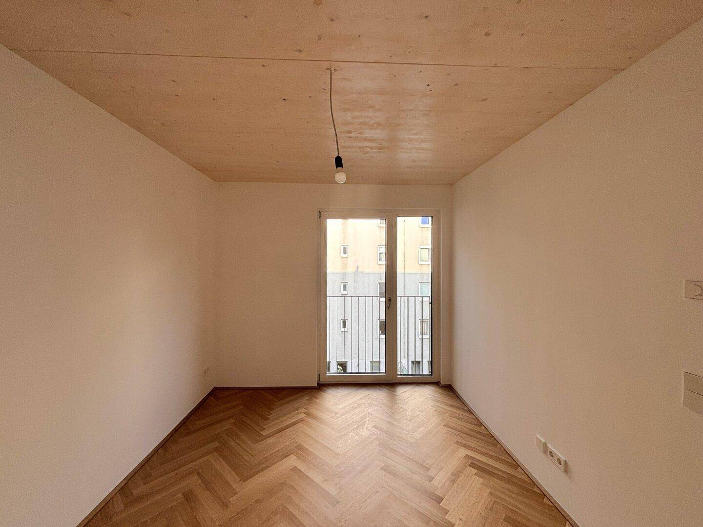 Heller Wohnraum mit Fischgrätparkett, Holzdecke und Blick auf die umliegenden Gebäude.