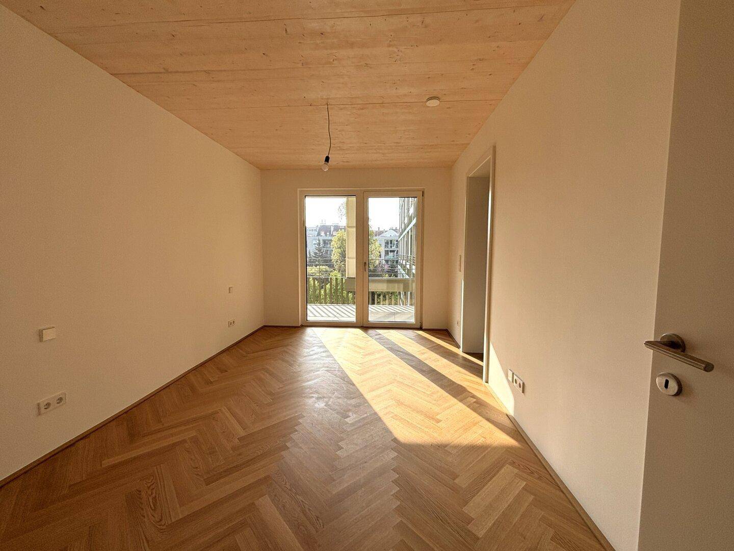 Sonniger Wohnbereich mit Fischgrätparkett, Holzdecke und Zugang zu einem Außenbereich.