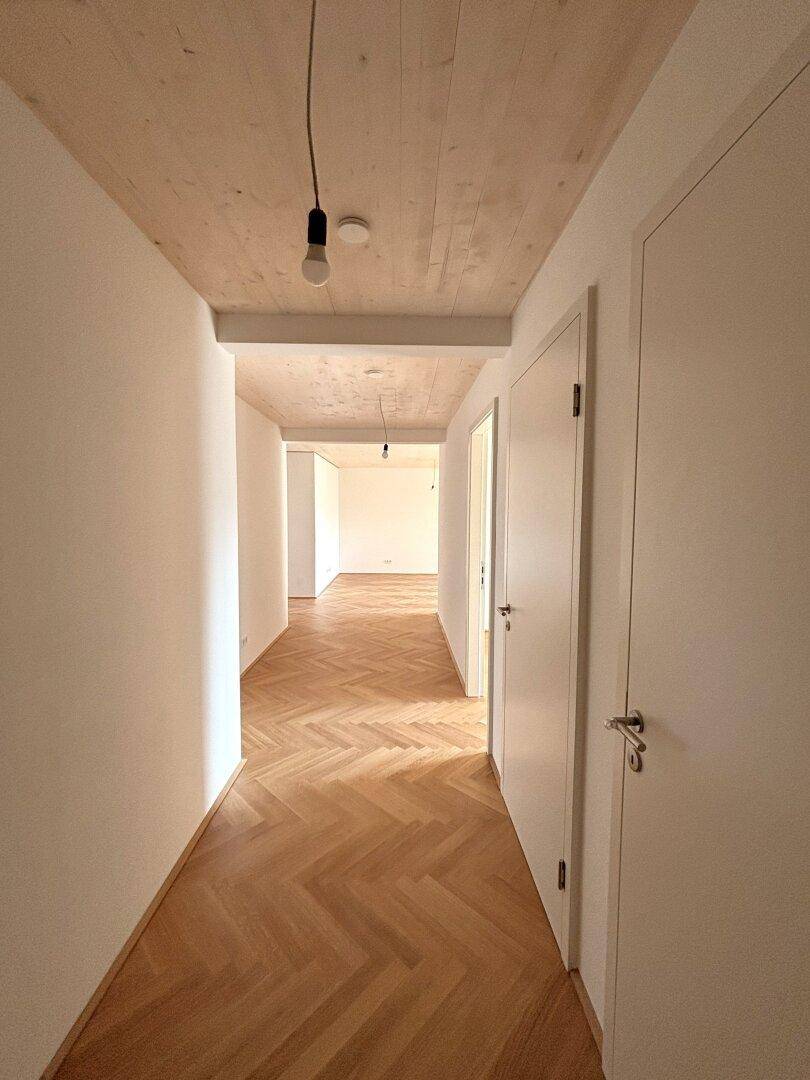 Langer, heller Flur mit Fischgrätparkett und Holzbalkendecke, der die Wohnbereiche verbindet.