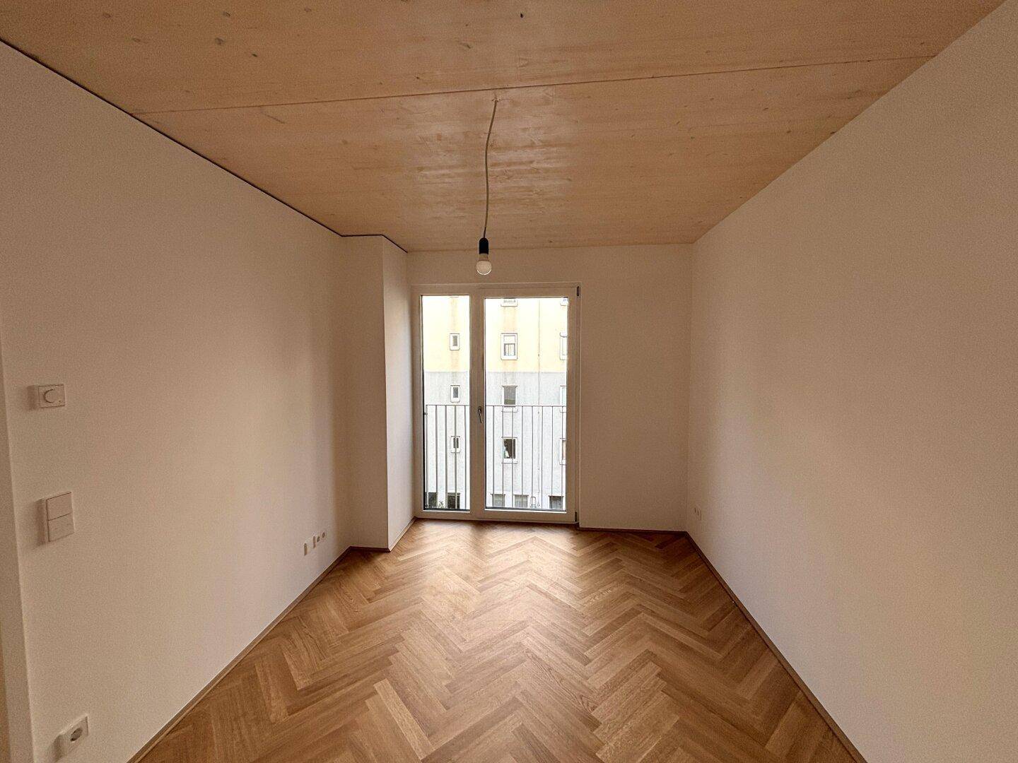 Ruhiges Schlafzimmer mit Fischgrätparkett, Holzbalkendecke und Blick auf die umliegenden Gebäude.