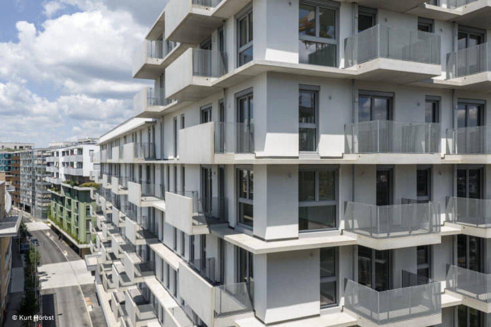 Detailansicht einer modernen Gebäudefassade mit vielen Balkonen und großen Fenstern.