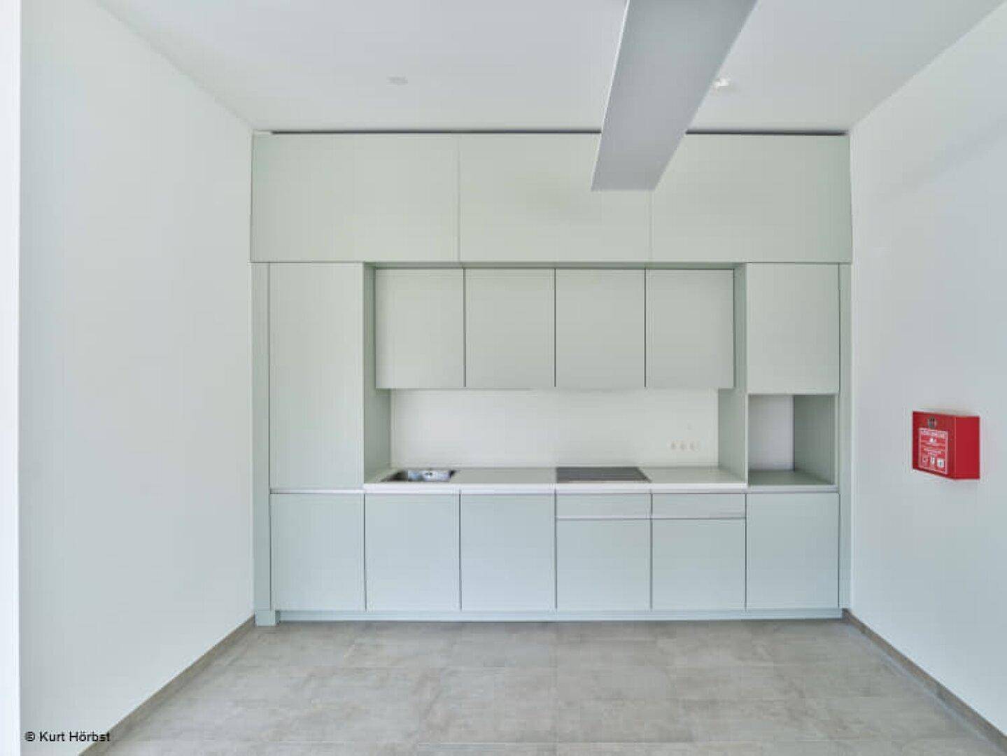 Moderne, ungenutzte Küchenzeile in hellem Mintgrün mit integrierten Geräten und Fliesenboden.