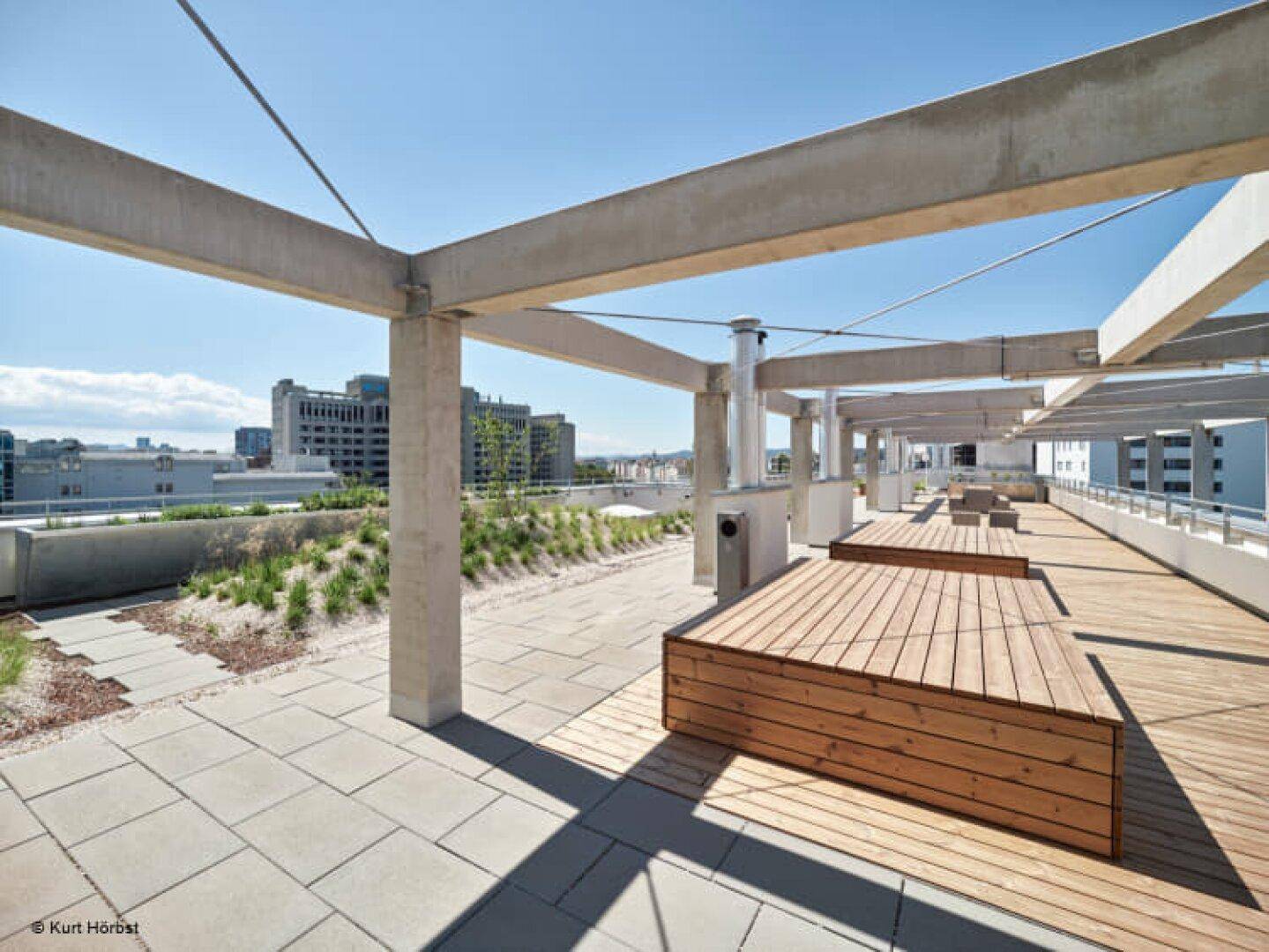 Geräumige Dachterrasse mit Holzdeck, Sitzgelegenheiten und Blick auf die Stadt.