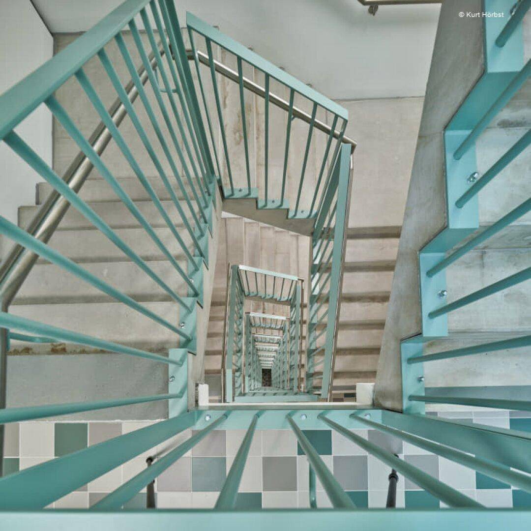 Modernes Treppenhaus mit hellblauen Geländern und gemustertem Fliesenboden.