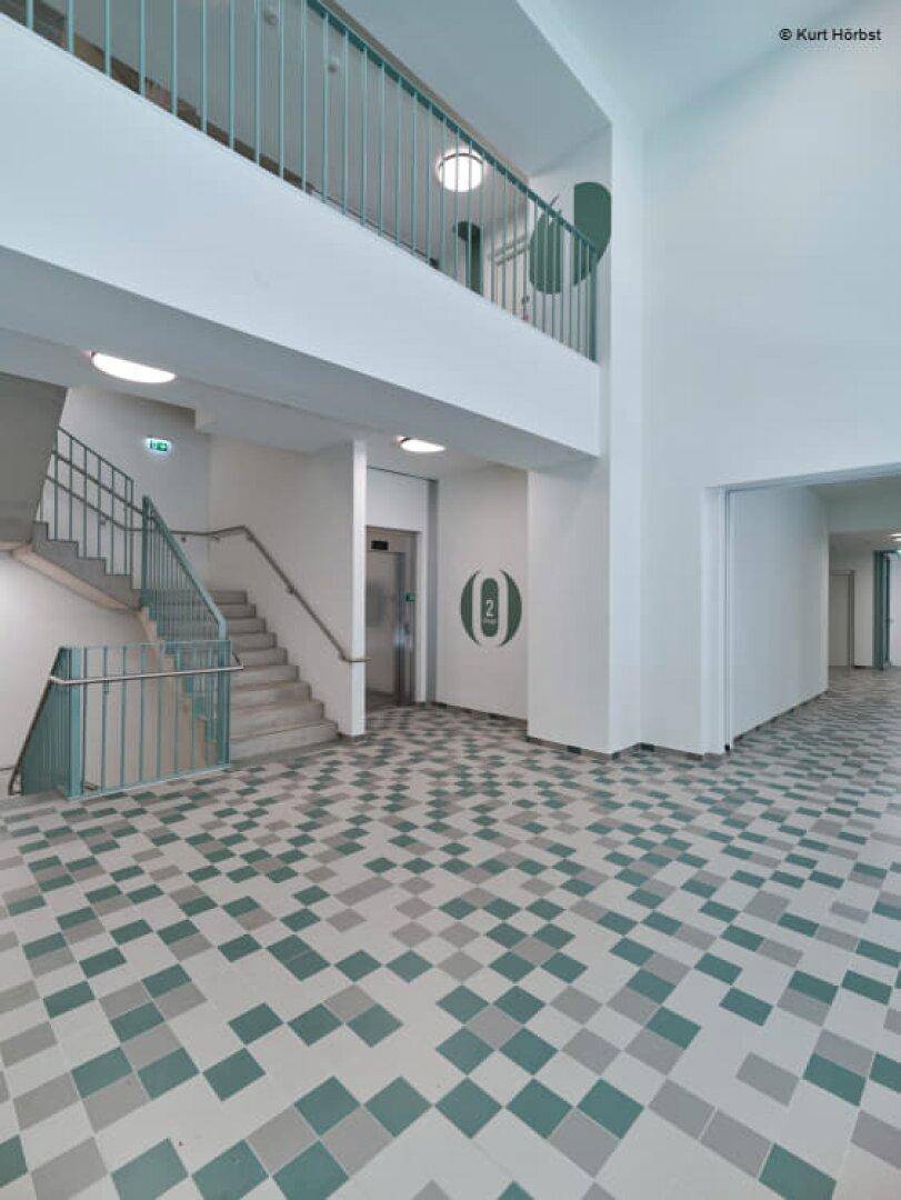 Geräumiger Eingangsbereich mit Fliesenboden, Treppenhaus und einem Aufzug.