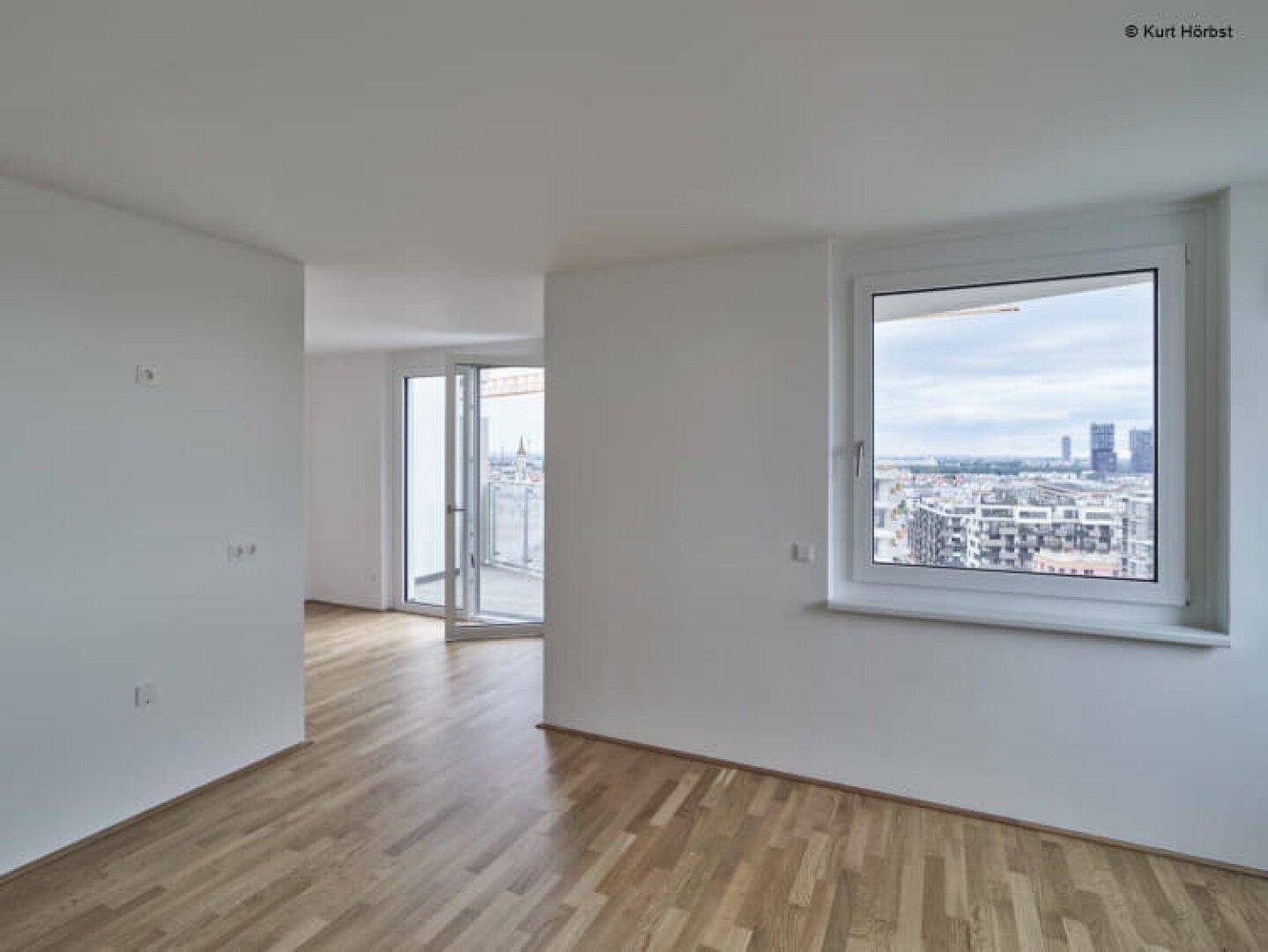 Helles Wohnzimmer mit Parkettboden und großen Fenstern, die einen weiten Stadtblick bieten.
