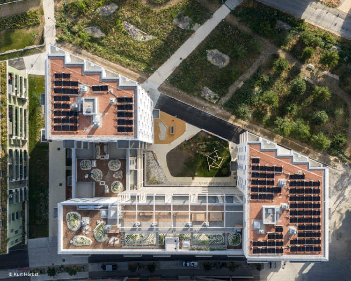 Luftaufnahme eines modernen Wohnkomplexes mit begrünten Dächern und Solaranlagen.