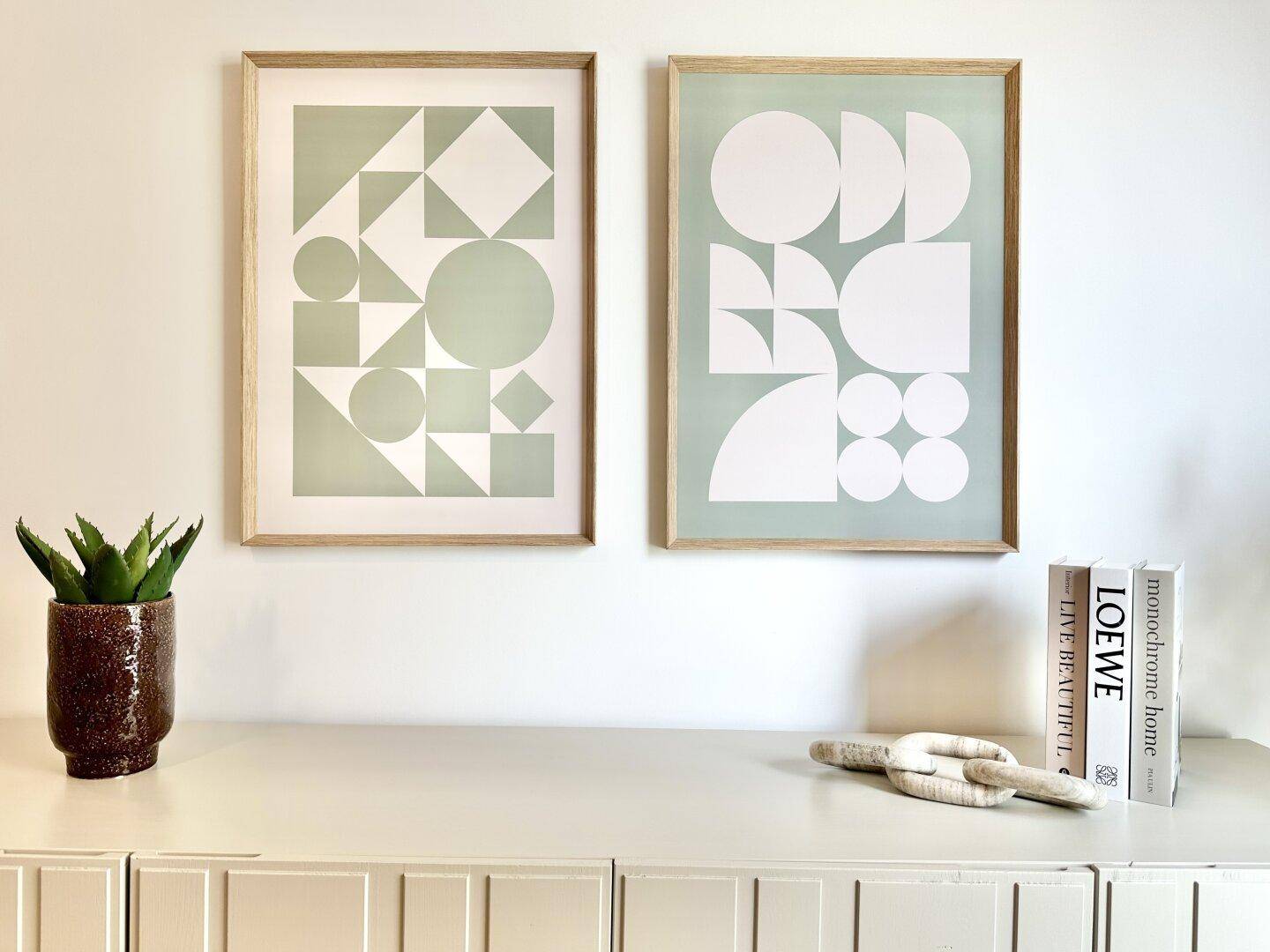 Moderne Kunstwerke mit geometrischen Mustern über einem Sideboard, ergänzt durch eine Pflanze und Bücher.