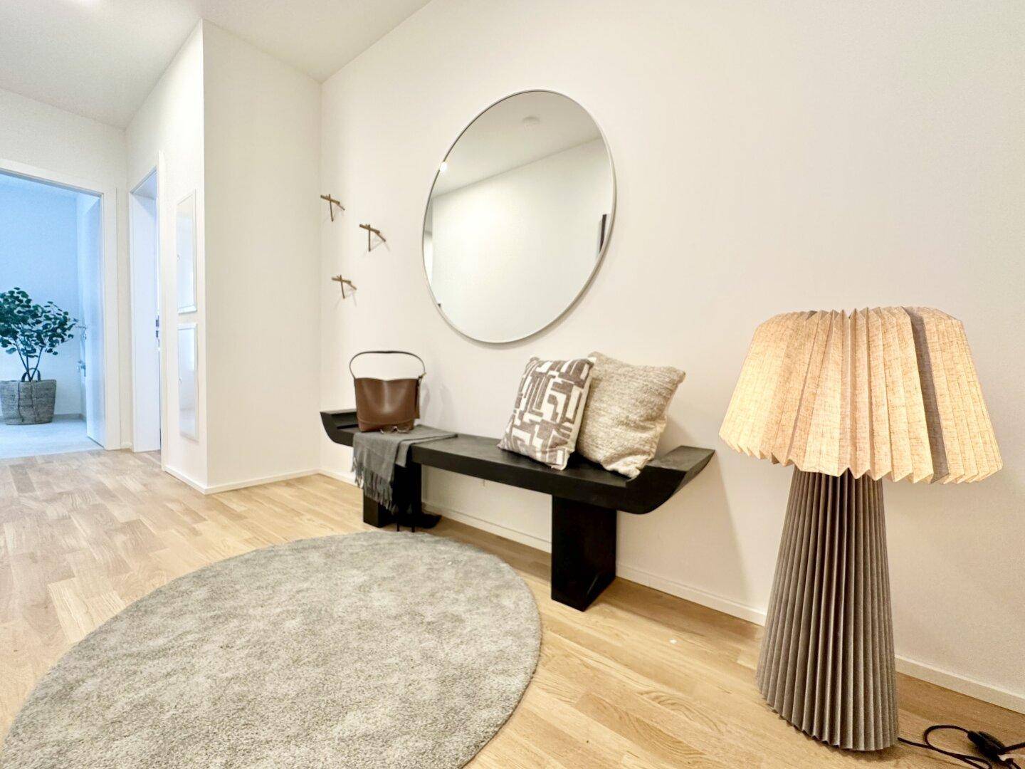 Heller Flur mit modernem Design, einem runden Spiegel, einer Sitzbank und einer stilvollen Stehlampe.