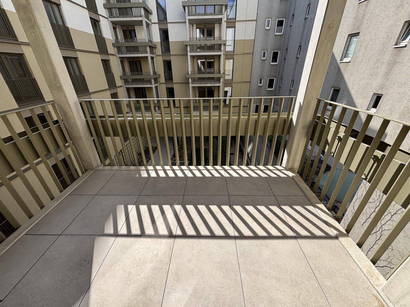 Heller Balkon mit Fliesenboden und Blick auf den Innenhof, ideal für entspannte Stunden.