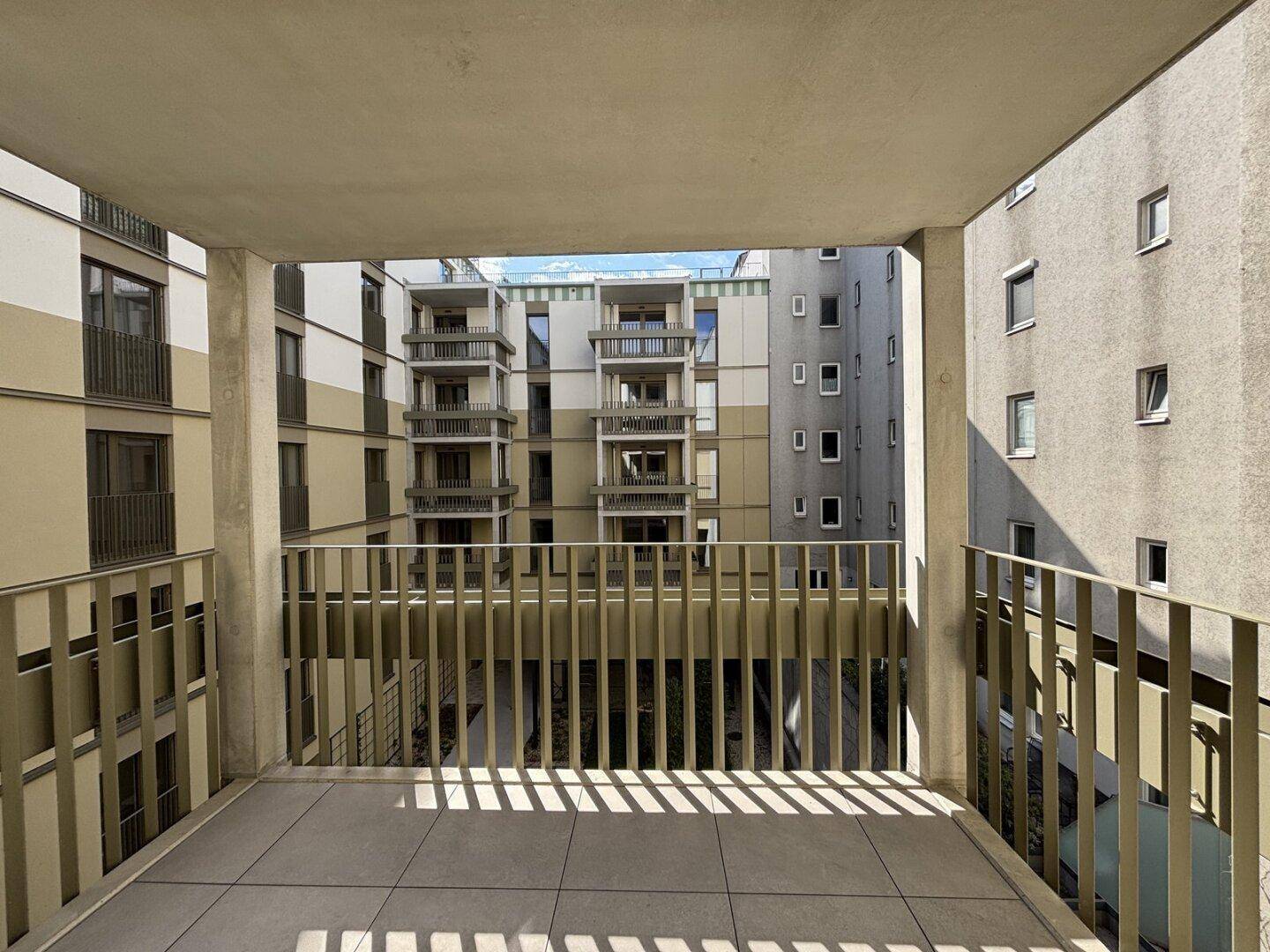 Balkon mit Blick auf den ruhigen Innenhof eines modernen Wohnkomplexes mit weiteren Balkonen.