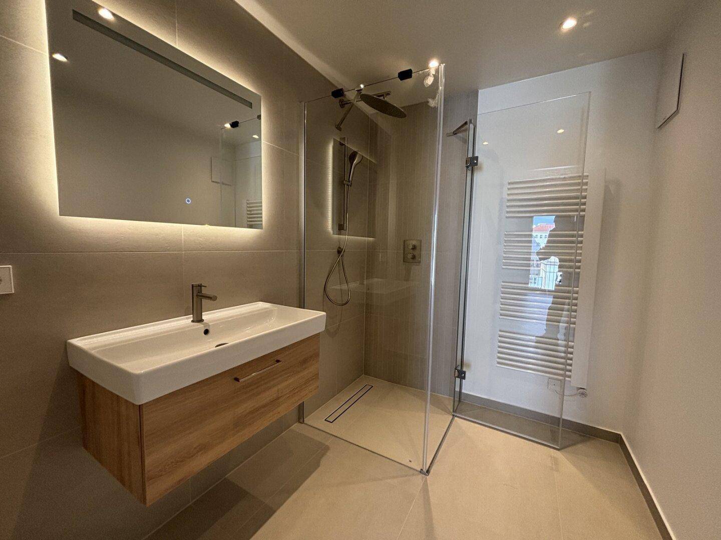 Modernes Badezimmer mit begehbarer Dusche, Waschtisch und beleuchtetem Spiegel.