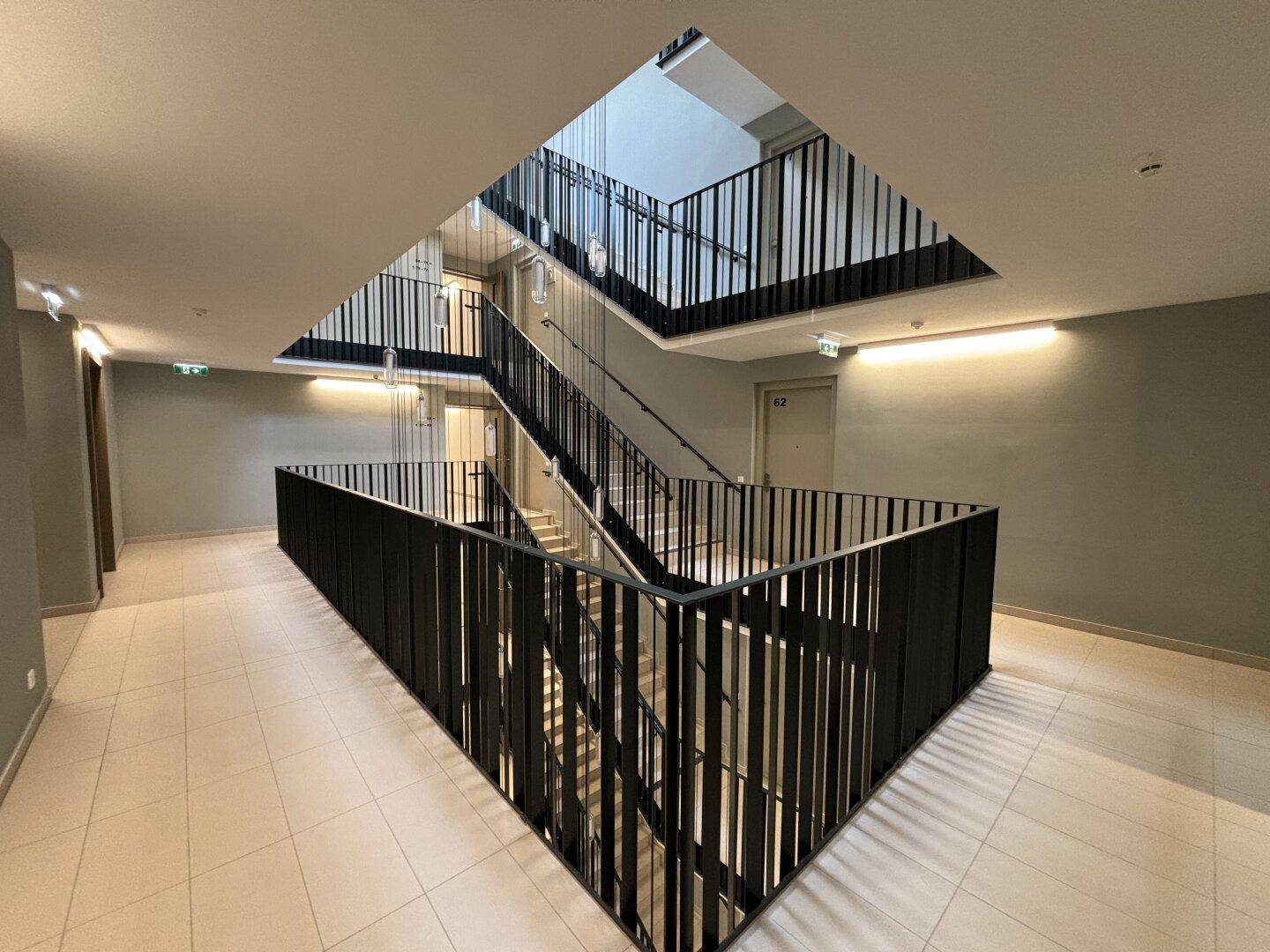 Modernes Treppenhaus mit schwarzem Geländer und hellen Fliesen in einem Mehrfamilienhaus.
