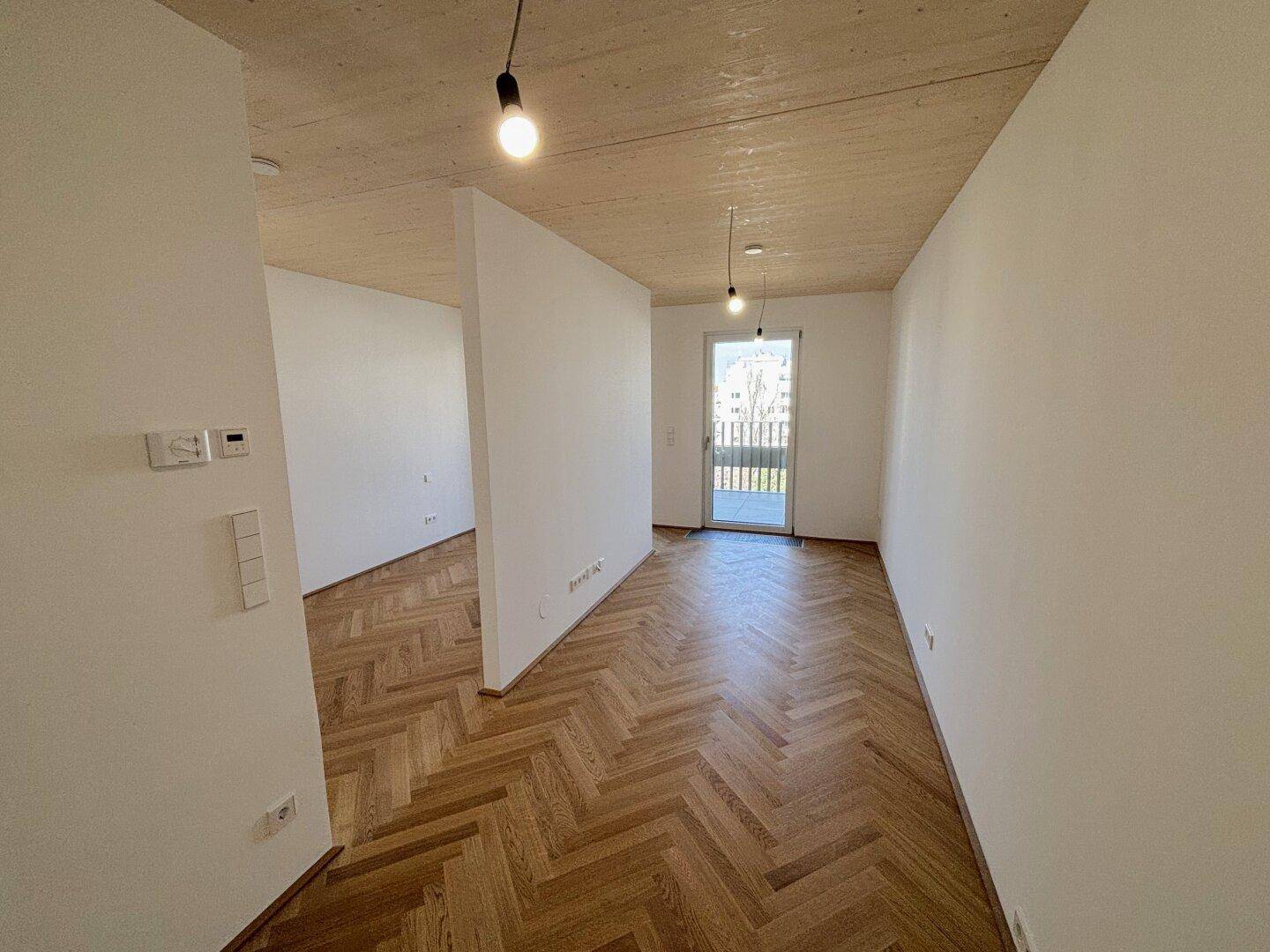 Heller Raum mit Fischgrätparkett, Holzdecke und Zugang zu einem Balkon, ideal als Wohn- oder Schlafzimmer.