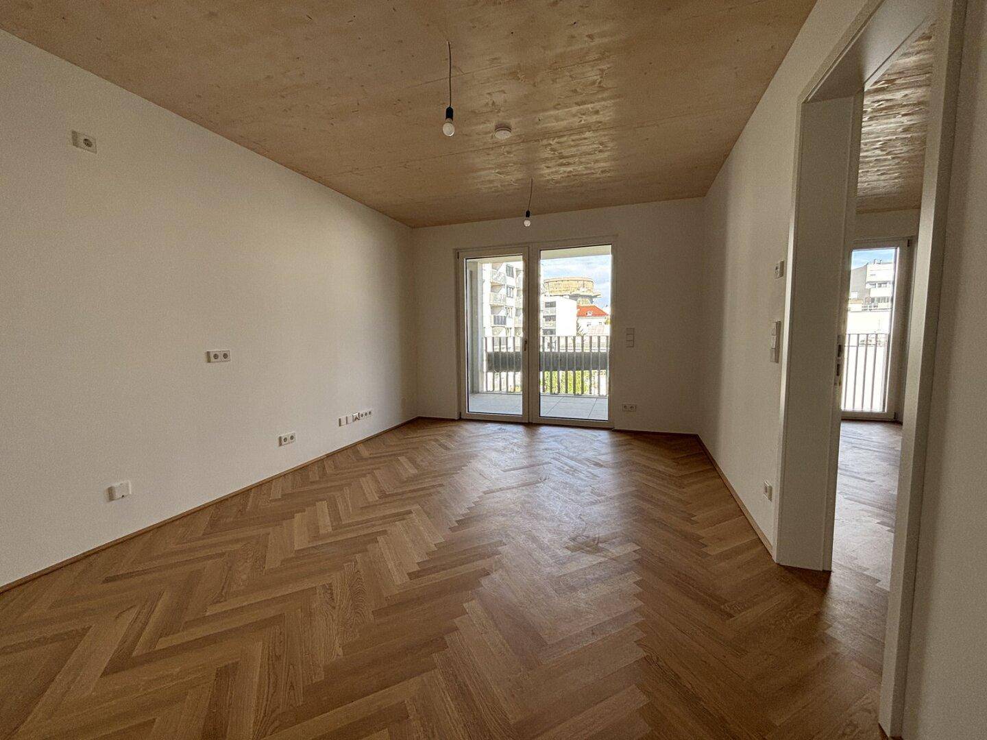 Heller Wohnraum mit Fischgrätparkett, Holzdecke und Zugang zu einem Balkon.