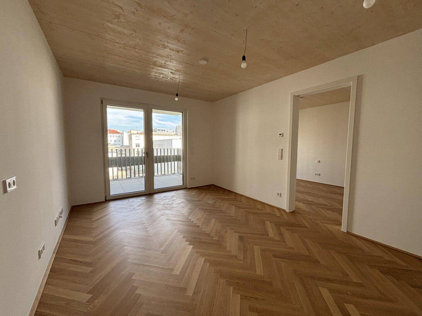 Unmöblierter Raum mit Fischgrätparkett, Holzdecke und Balkonzugang.