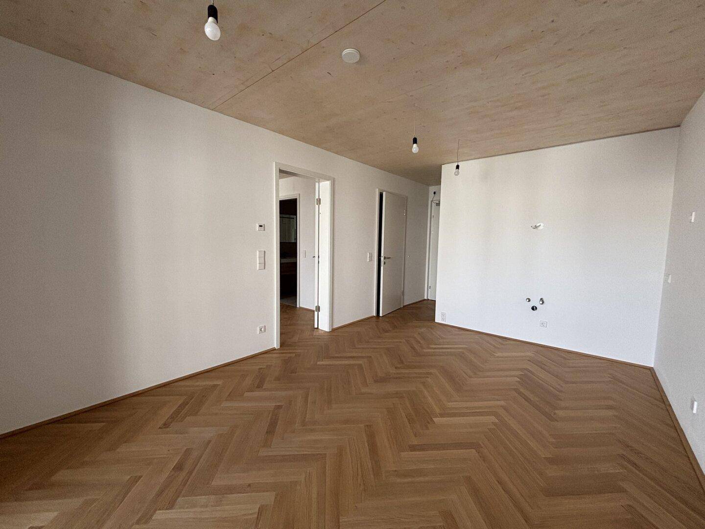 Helles Zimmer mit Fischgrätparkettboden und mehreren Türen, bereit für die Einrichtung.