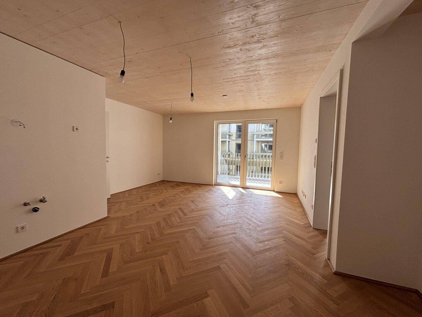 Heller Wohnraum mit Fischgrätparkett, Holzdecke und Zugang zu einem Balkon oder einer Terrasse.