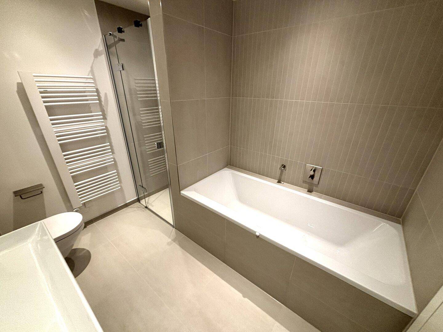 Modernes Badezimmer mit integrierter Badewanne, Duschbereich und beheiztem Handtuchhalter.