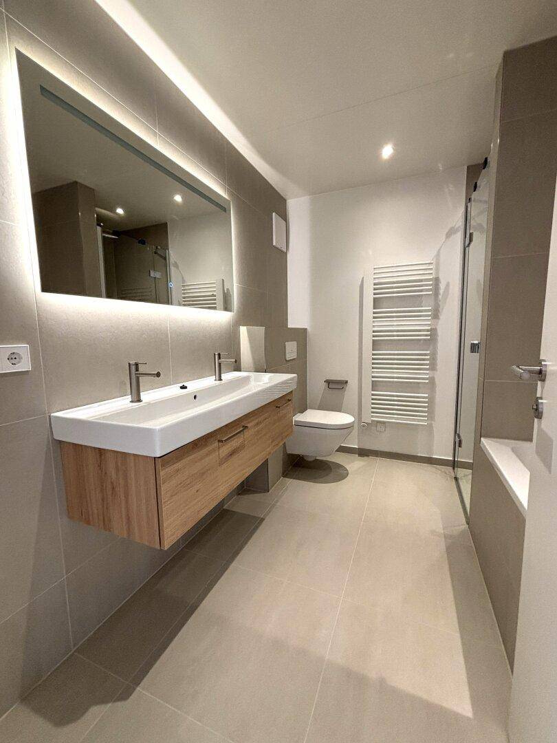 Helles Badezimmer mit Doppelwaschbecken, beleuchtetem Spiegel und wandhängendem WC.
