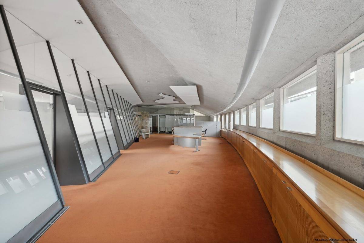 Weitläufiger Bürobereich mit Teppichboden, integrierten Schränken und einer geschwungenen Fensterfront.