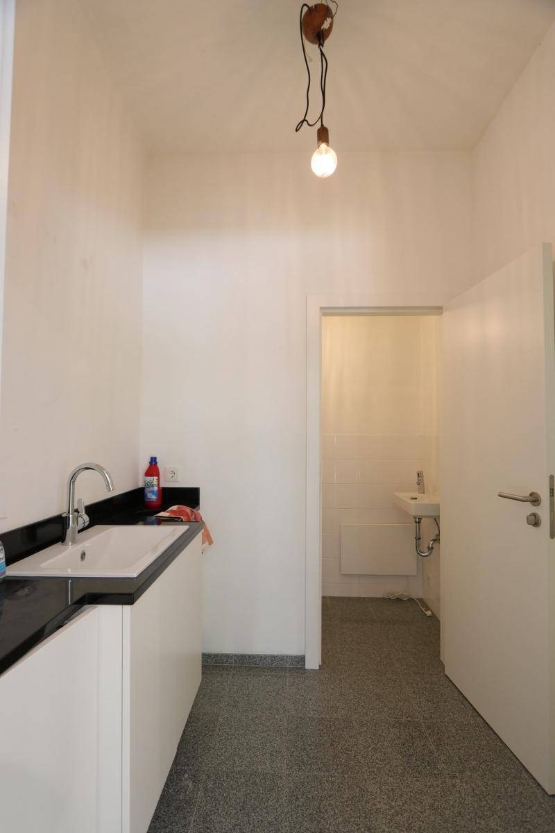 Funktionaler Hauswirtschaftsraum mit Waschbecken, dunkler Arbeitsplatte und Zugang zu einer separaten Toilette.